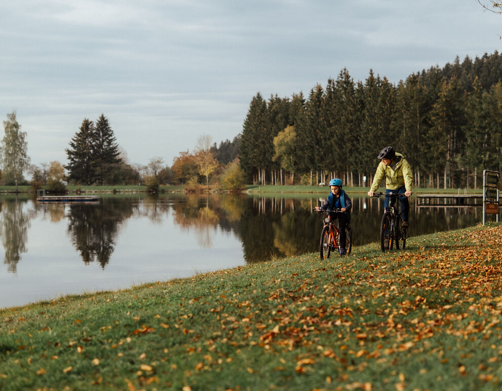 Vater und Sohn fahren mit Rad an Badesee-Ufer; herbstliche Stimmung;